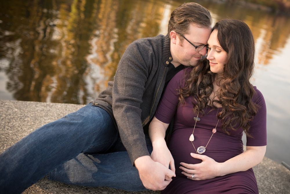 Maternity couple sitting together by a peaceful pond.